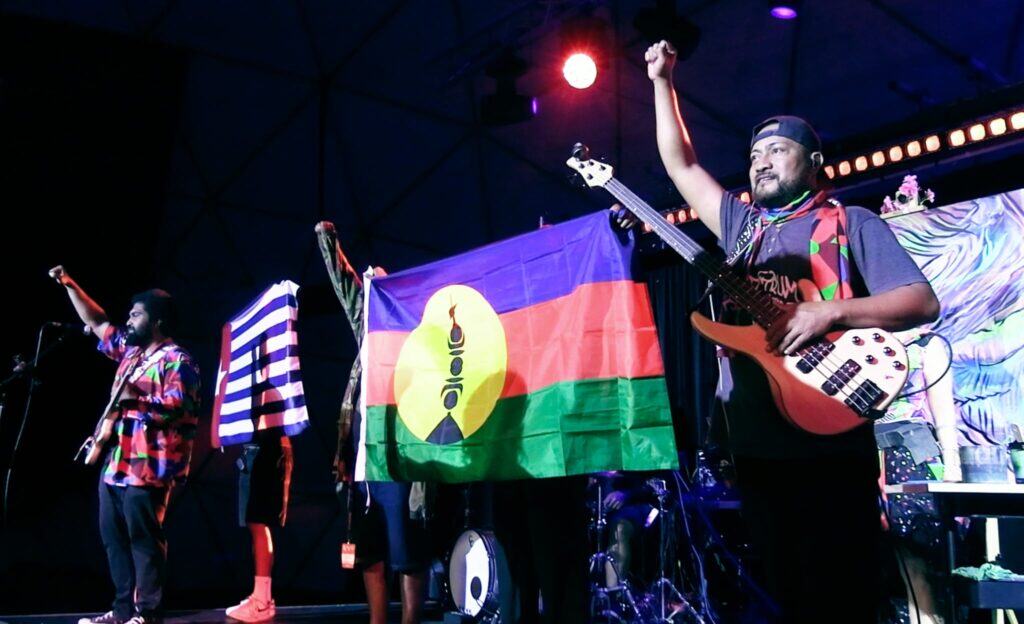 People stand on stage flanked by Kanaky abd West Papua flags