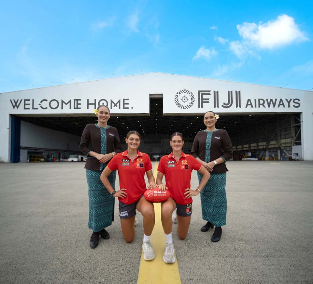 Four people standing and kneeling in front of aircraft hanger